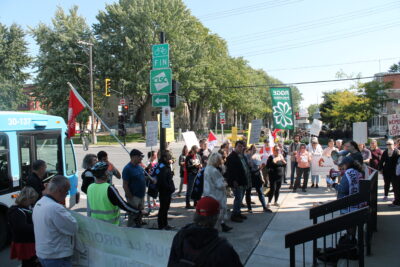 Une petite foule devant les bureaux de la ministre Chantal Rouleau. Les participantEs tiennent différentes pancartes et bannières avec les logos de leurs organismes ou des slogans revendiquant l'indexation.